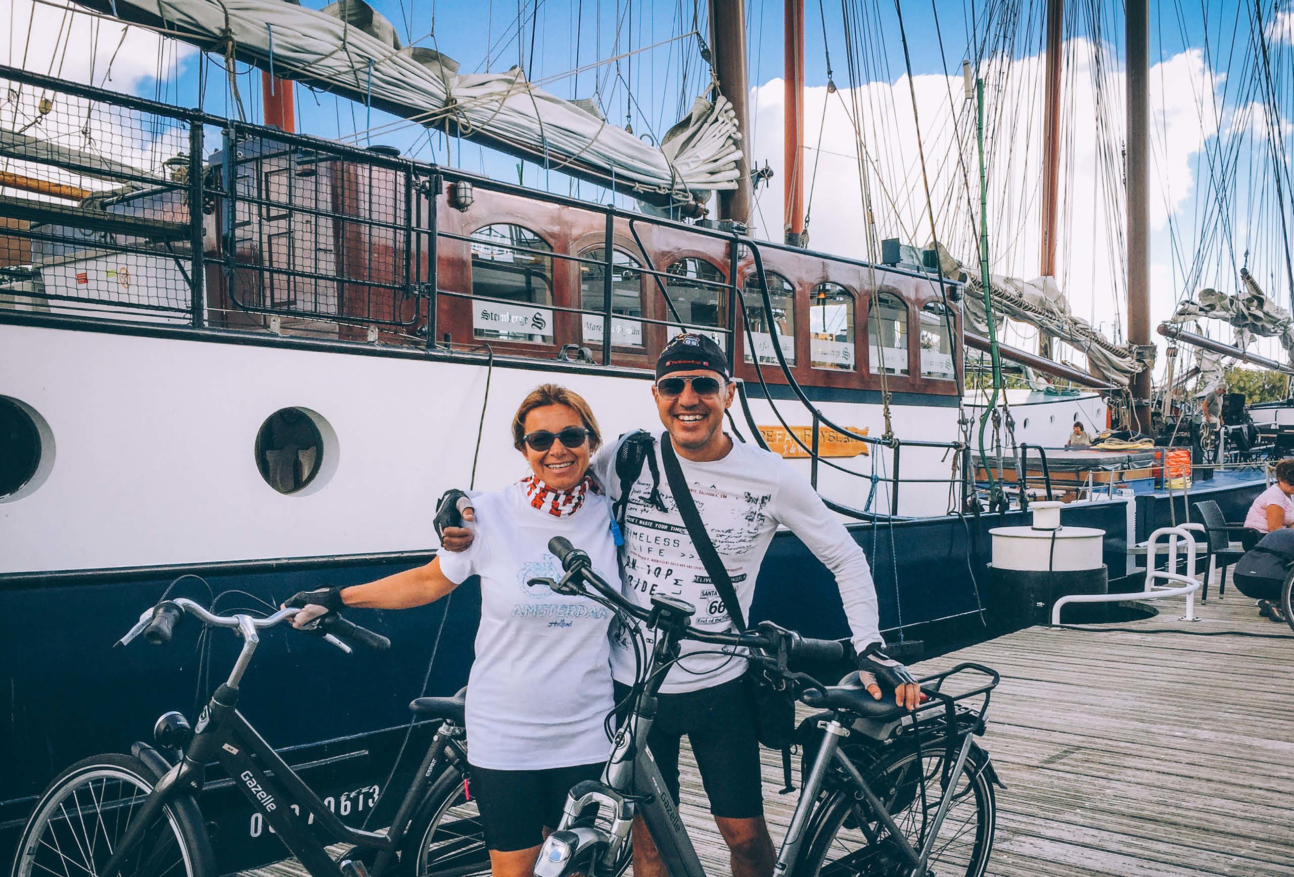 Radfahrerpaar vor einem historischen Segelschiff im Hafen, Niederlande.