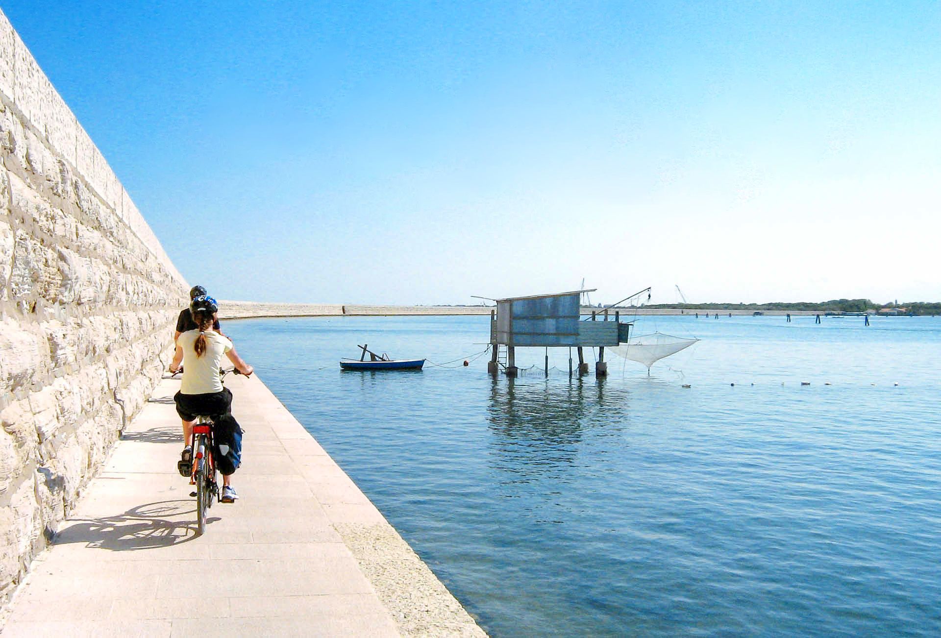 Ciclisti in viaggio su ciclabile vicino alla diga, viaggi in bici e barca da Venezia a Mantova
