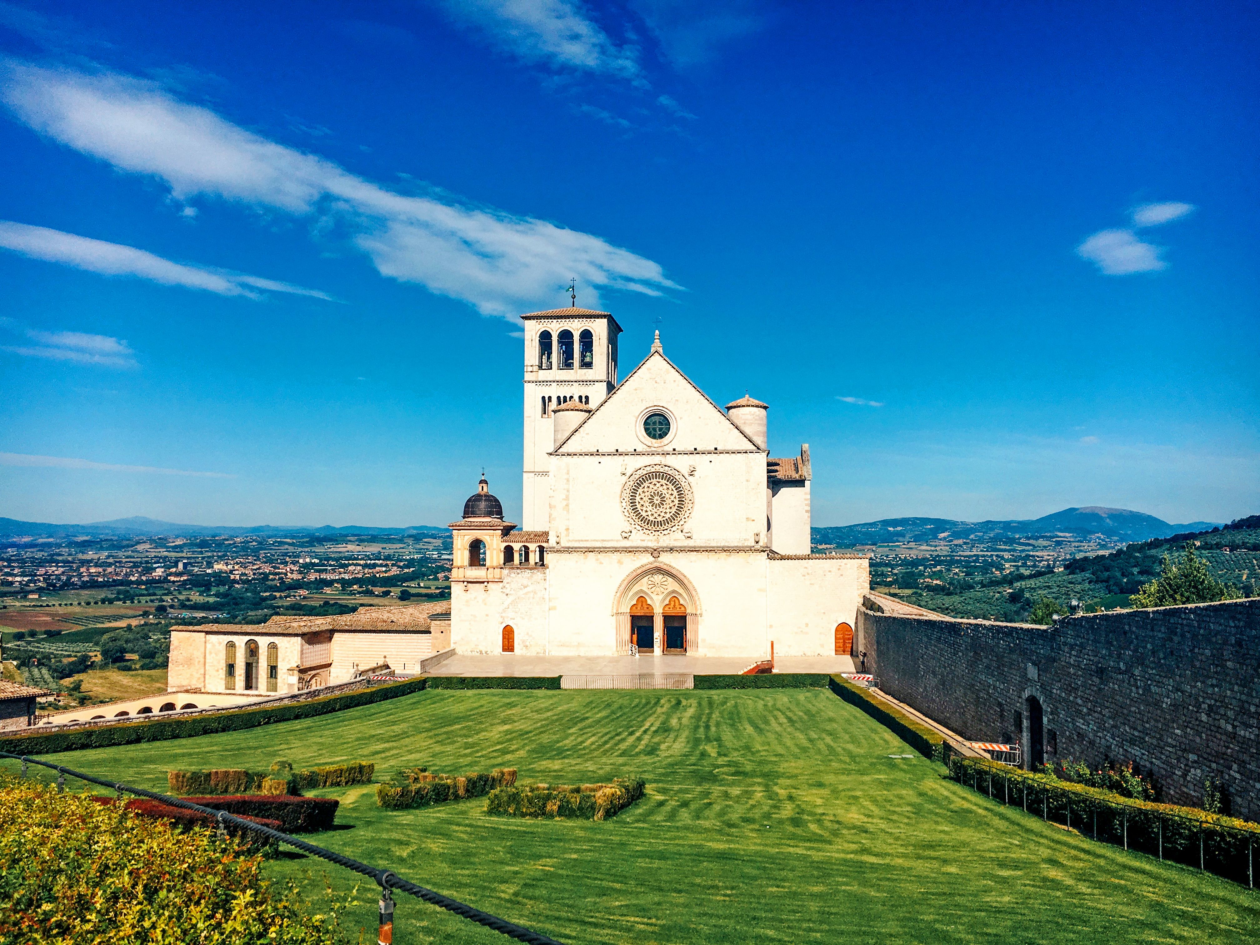 Fassade der Basilika des Heiligen Franziskus in Assisi mit grünem Rasen und blauem Himmel.