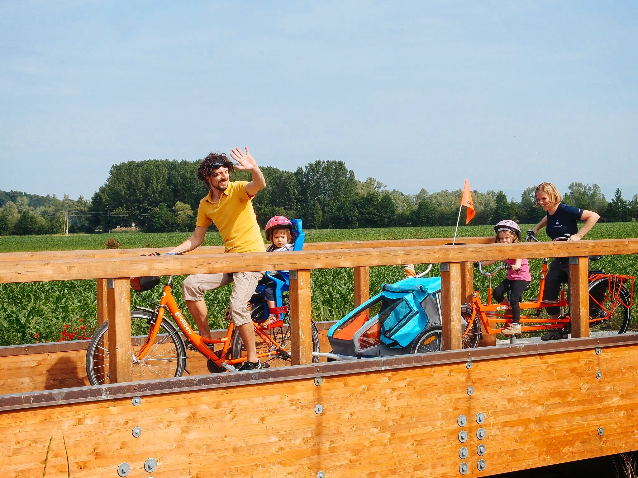 Menschen überqueren eine Holzbrücke mit Weinbergen im Hintergrund, Euganeische Hügel, Familienradurlaub