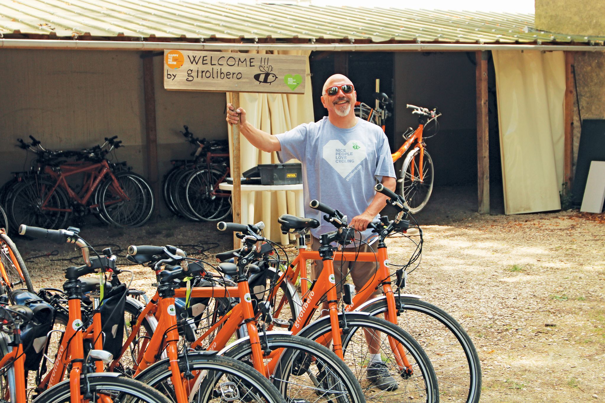 Smiling gentleman posing behind a row of orange bicycles "Girolibero", tour operator, bike tour organisation