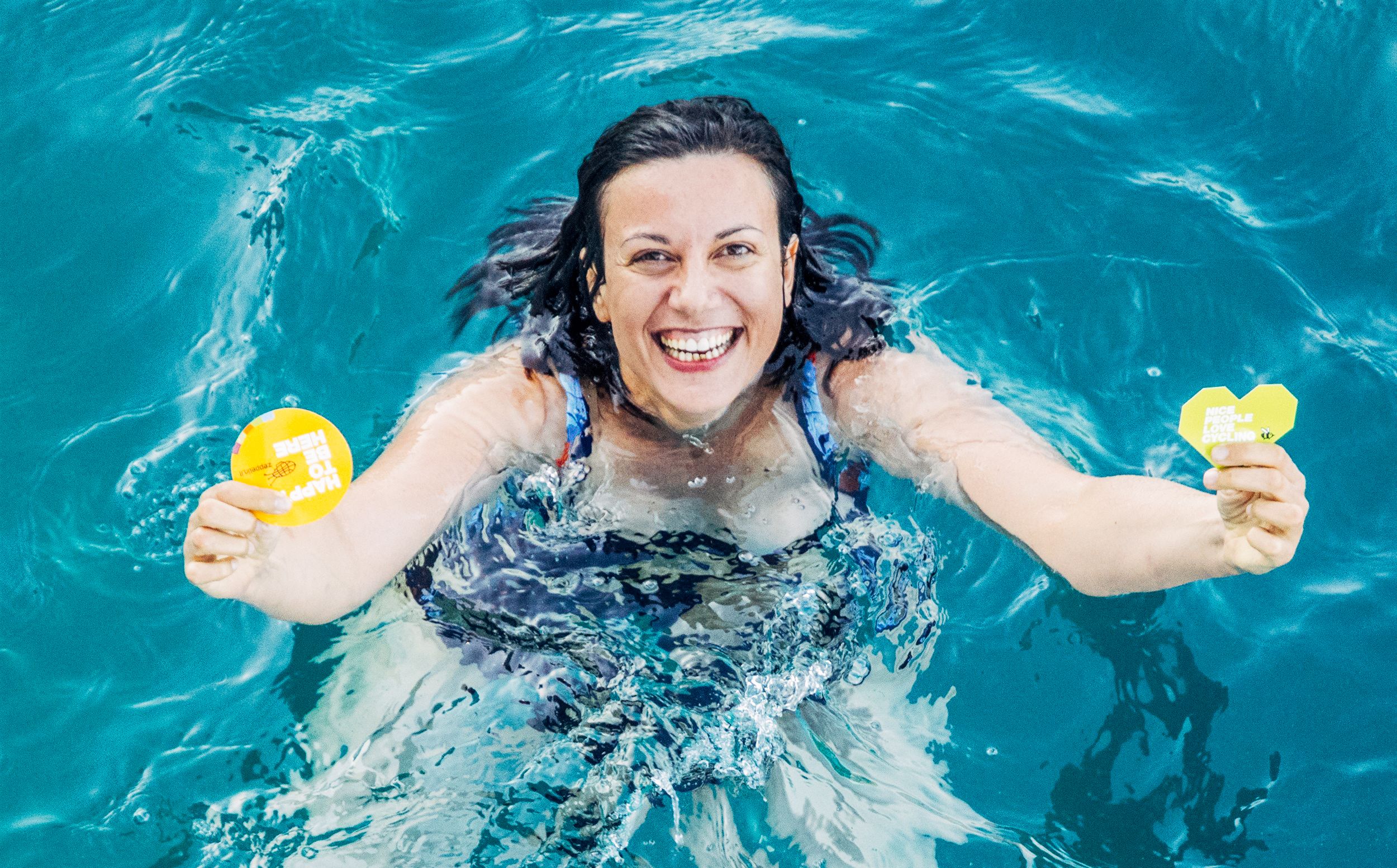 Lächelnde Person in einem Pool, die zwei Gummienten hält
