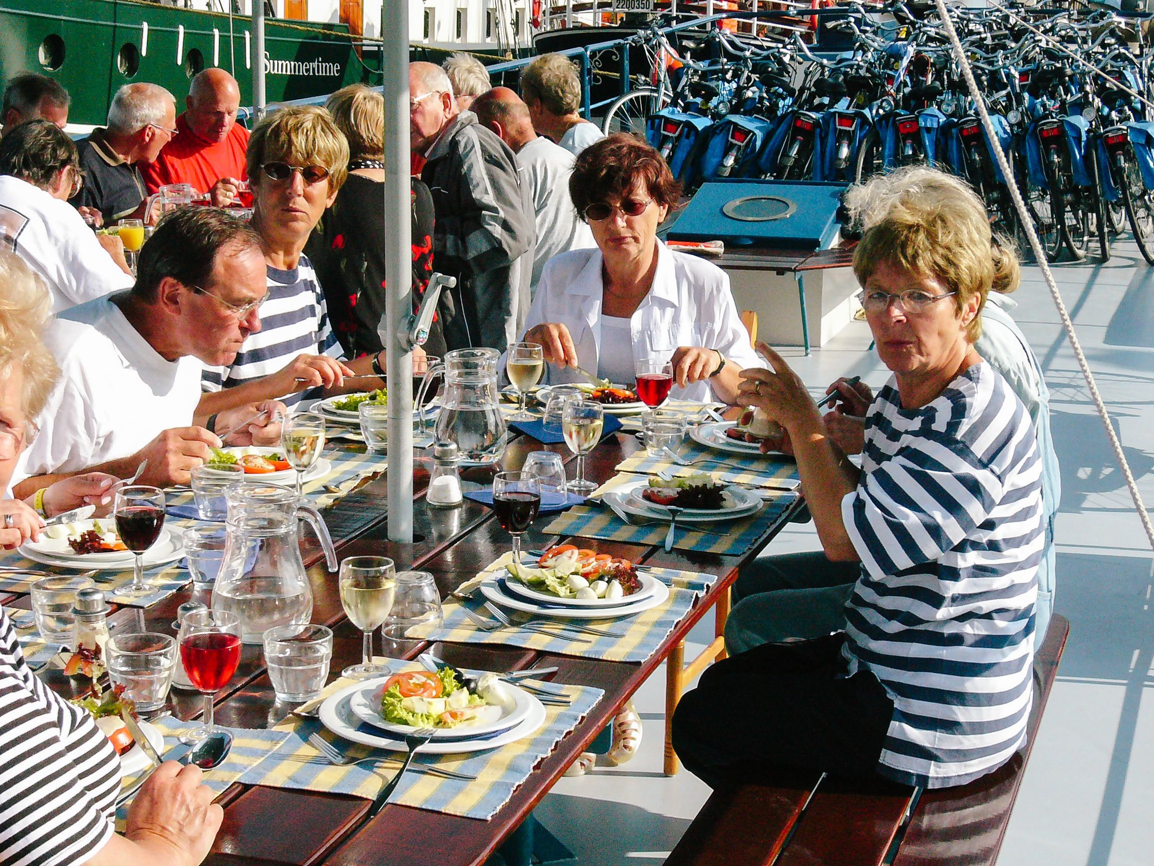 Menschen beim Mittagessen auf dem Deck eines Touristenbootes auf einem Kanal in Amsterdam mit Tischen im Freien