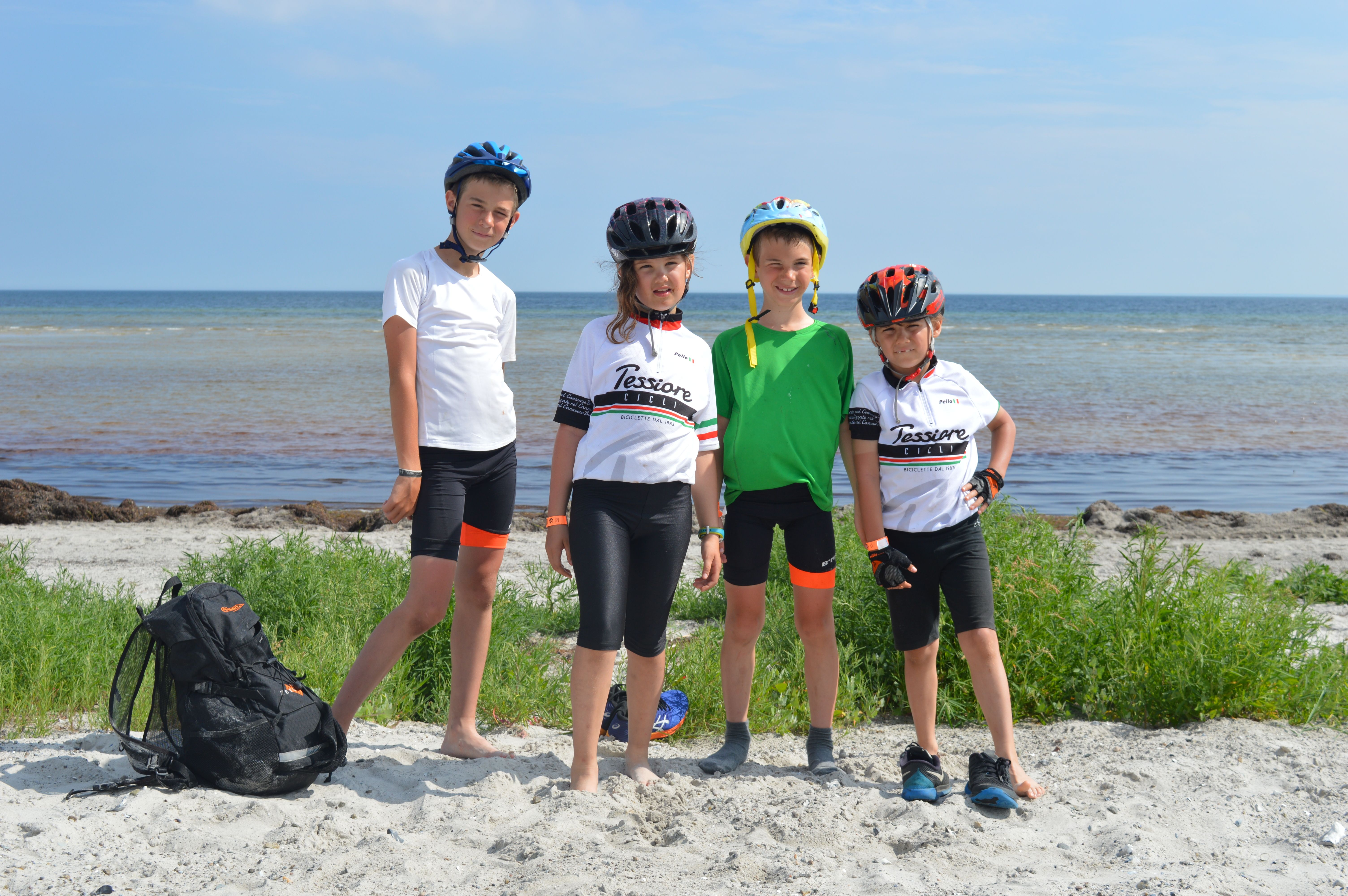 Ragazzi con abbigliamento e caschetto vicino al mare in Danimarca, con biciclette parcheggiate sulla spiaggia, viaggi in bici per famiglie