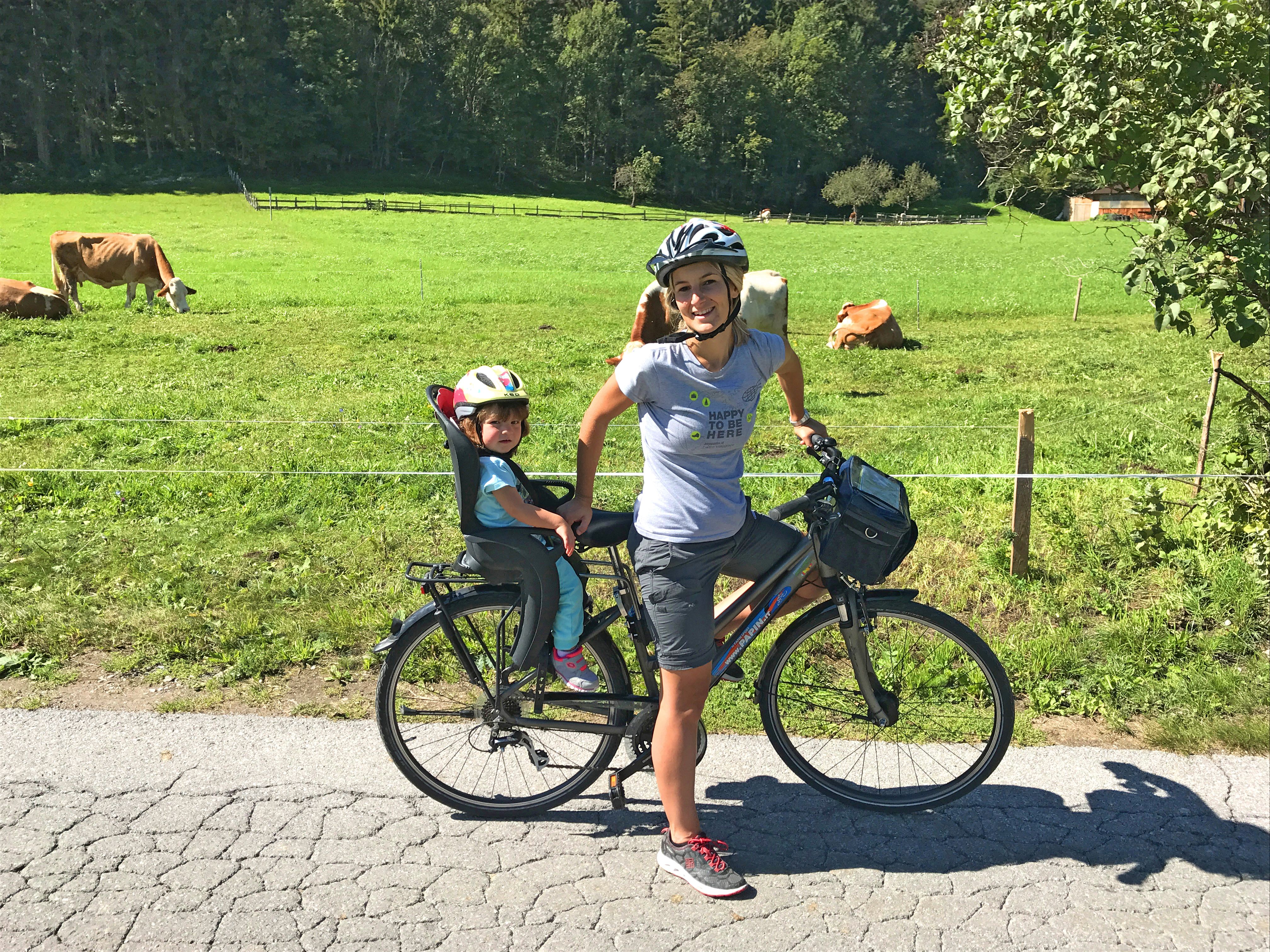 Famiglia in bicicletta attraverso i prati verdi di Villach, Carinzia, tra mucche al pascolo nei prati e boschi