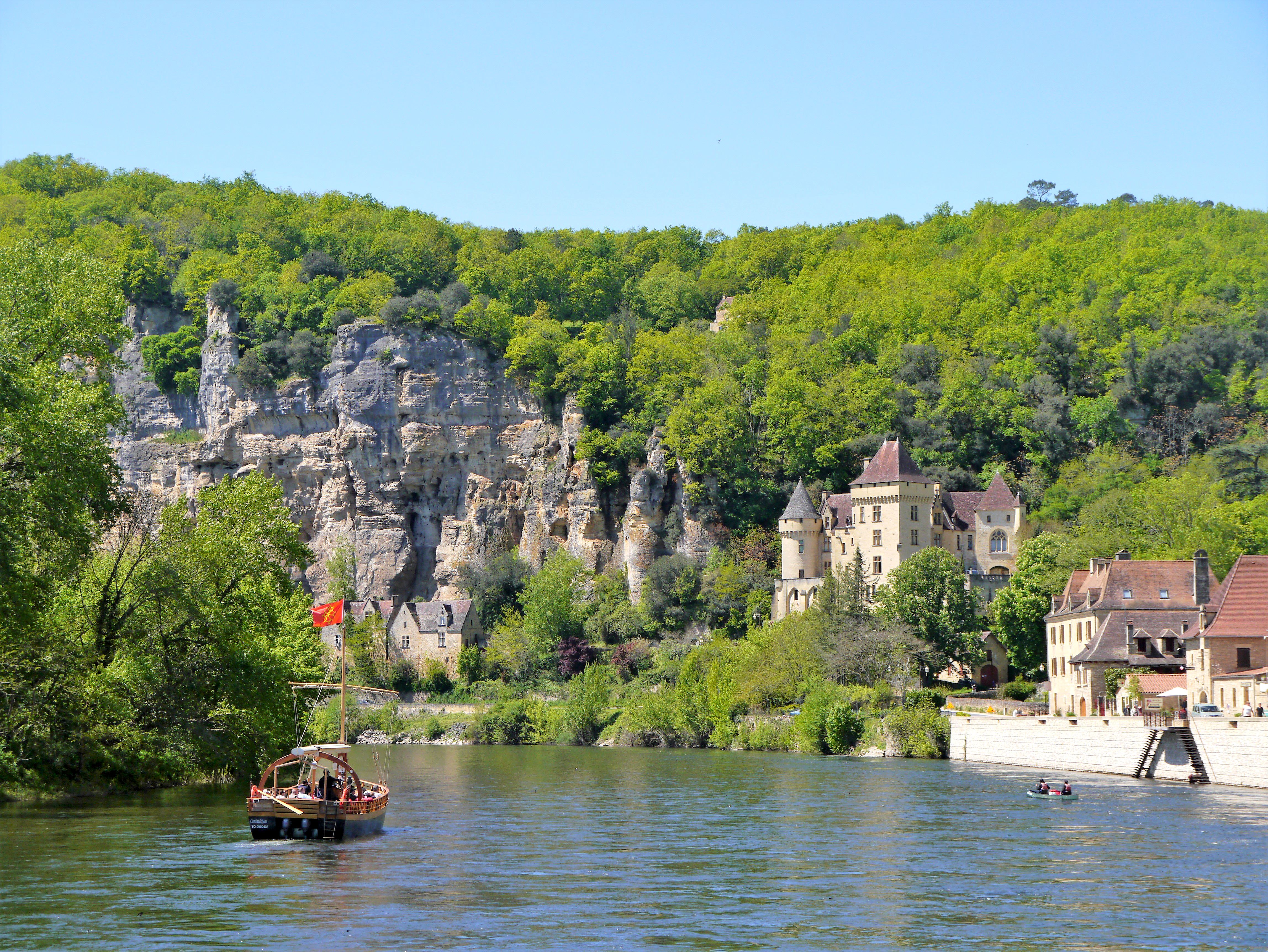 Barca sul fiume Dordogna che passa davanti al villaggio di La Roque-Gageac circondato da colline verdi, Francia