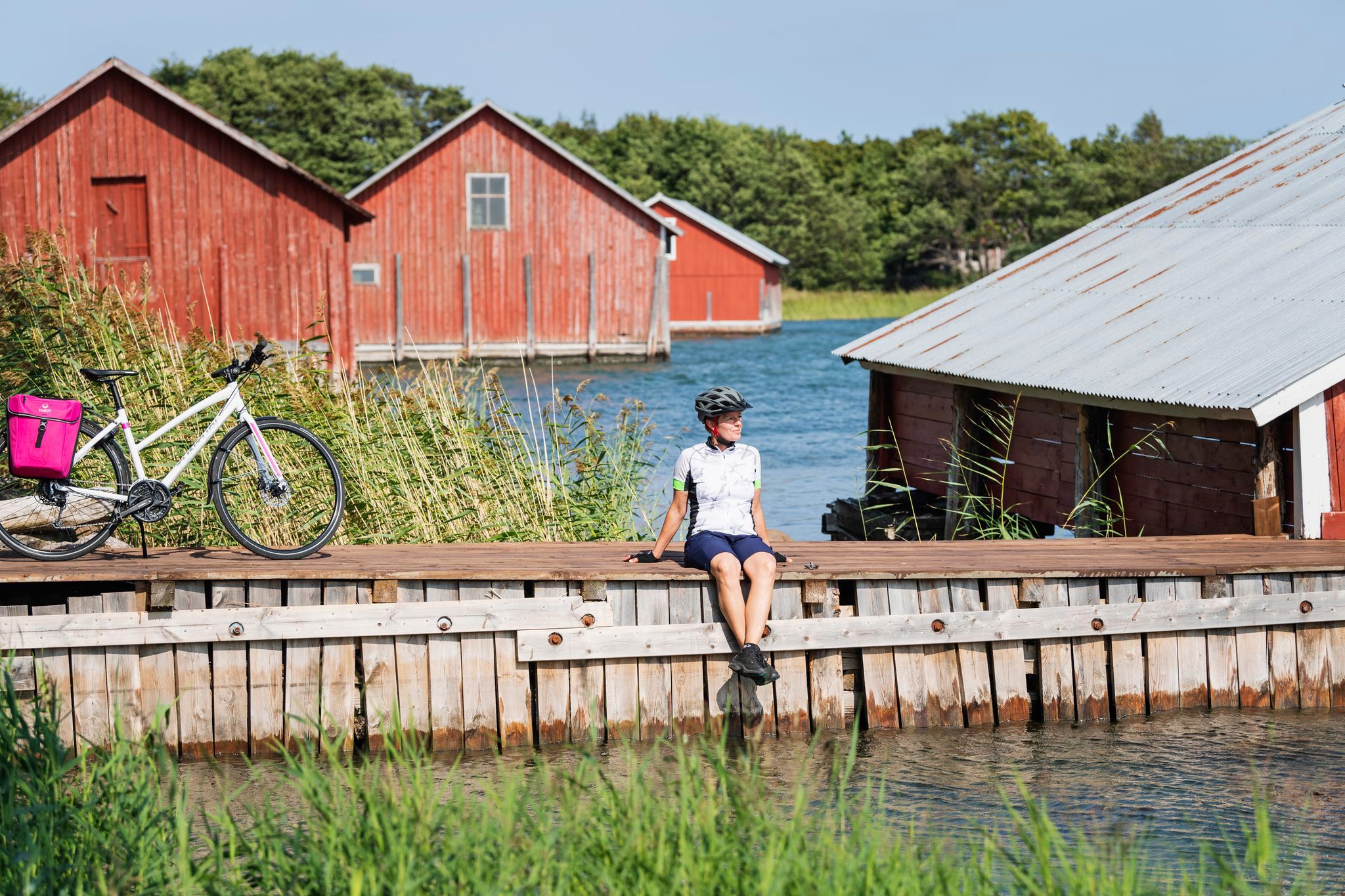 Cicloturista seduto davanti a un tipico edificio rosso in legno con una terrazza sul mare, nell'arcipelago di Turku.