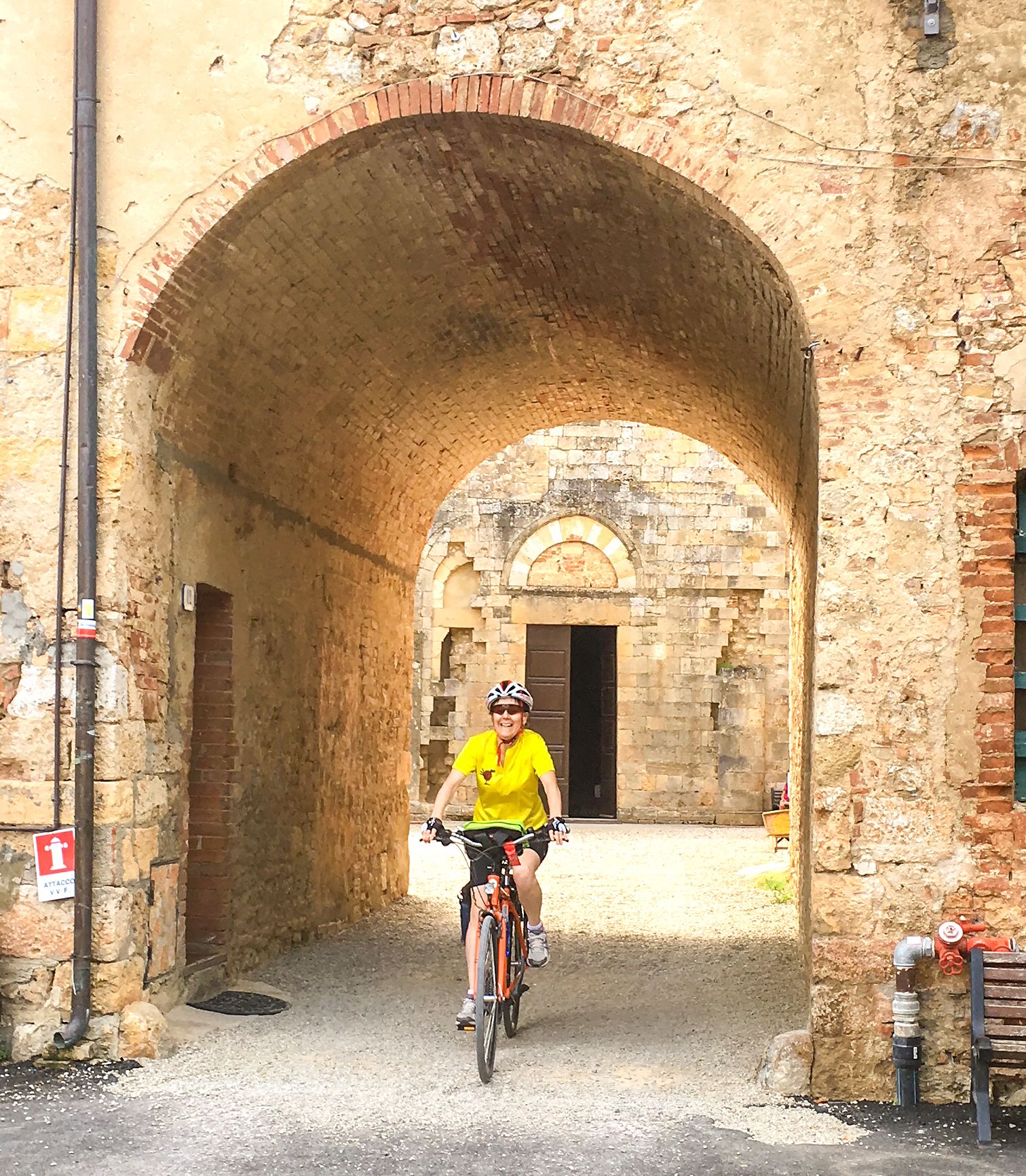 Ciclista che attraversa un arco storico in un borgo toscano.