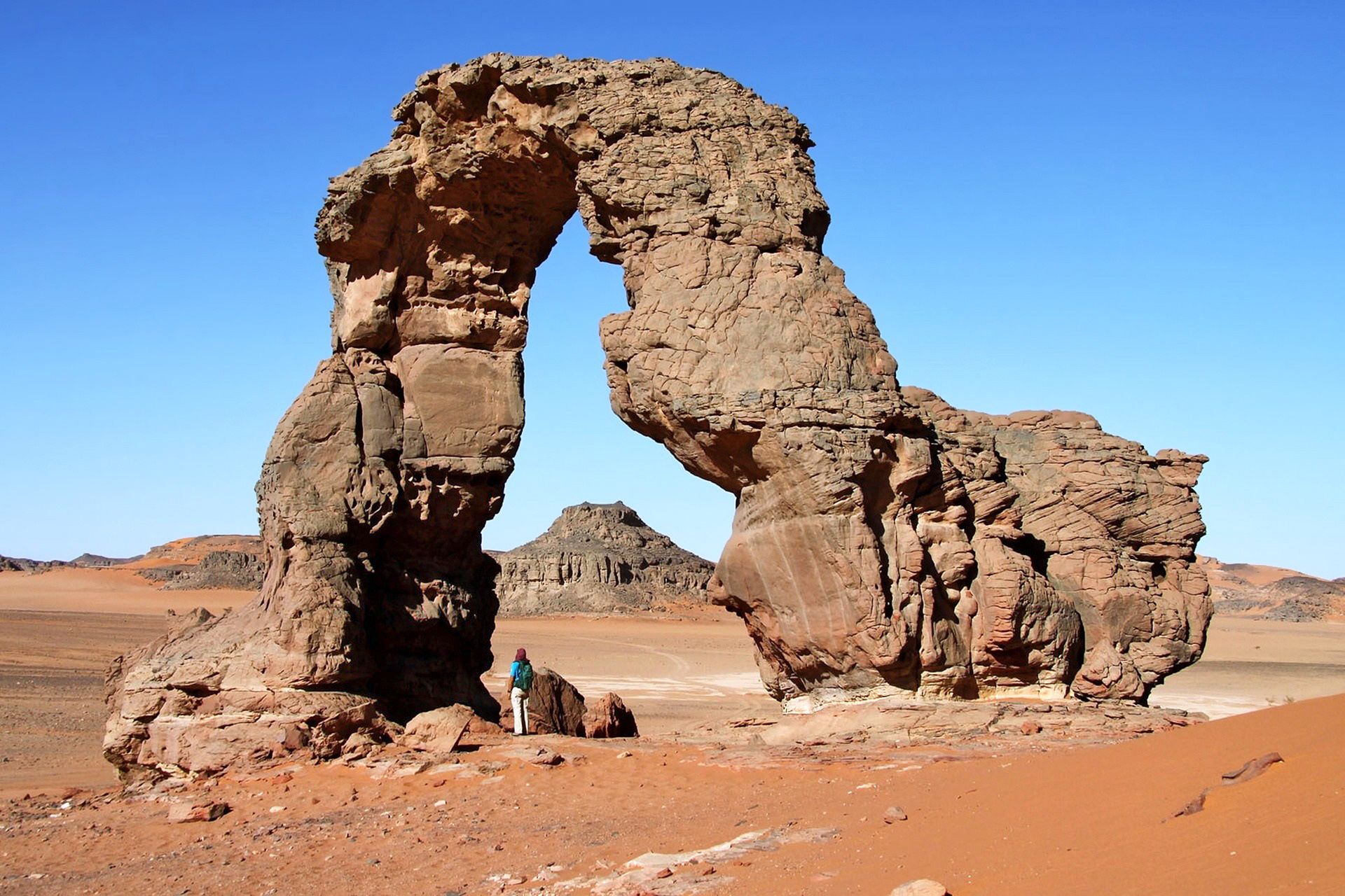 Formazione rocciosa naturale ad arco nel deserto del Sahara, circondata da paesaggi aridi e cielo limpido.