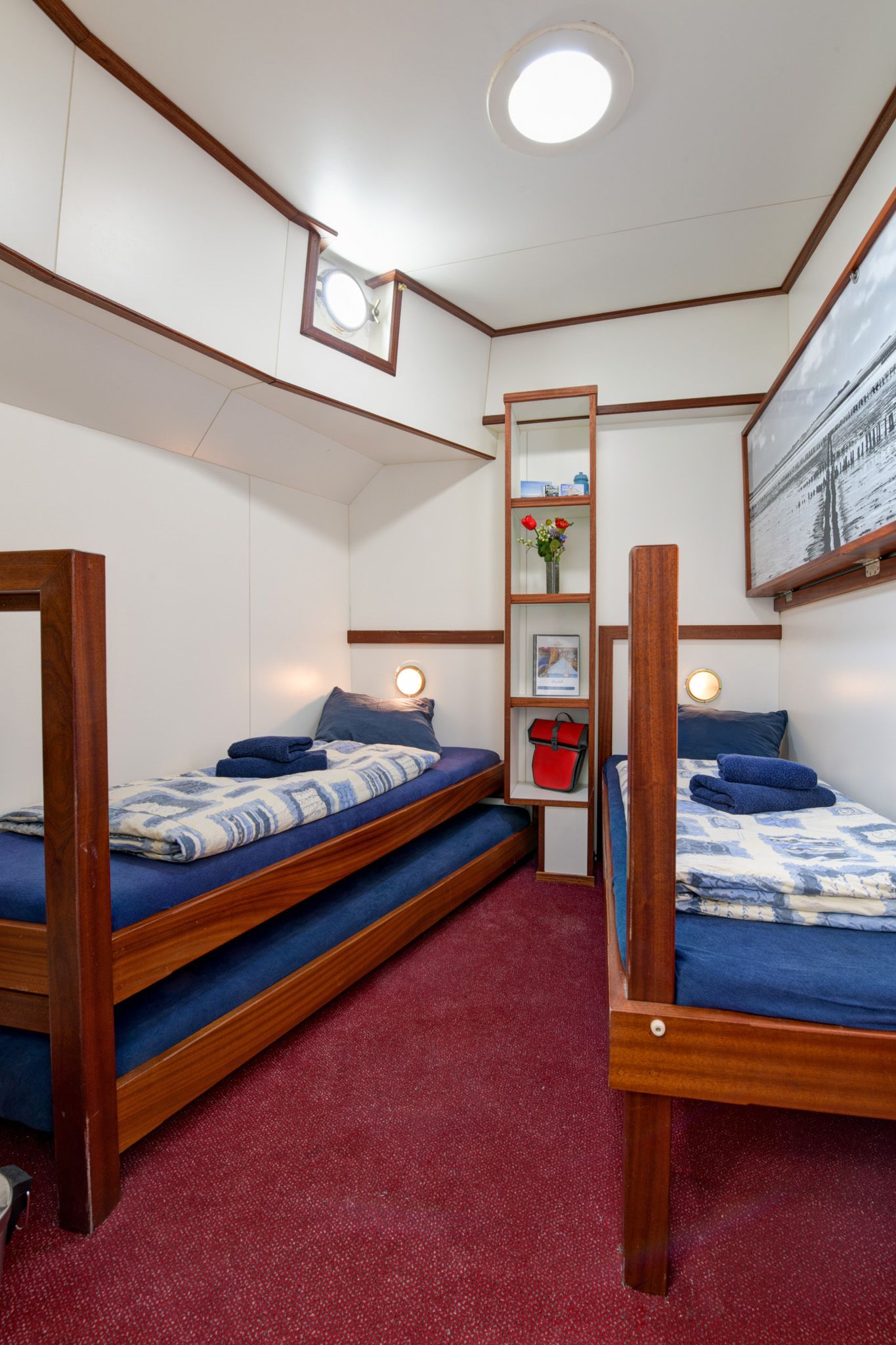 Cabina con letti a castello in legno, interni accoglienti con moquette rossa e oblò.