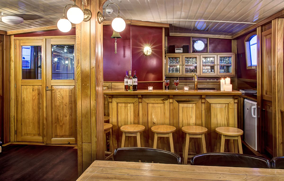 Salone interno con bar in legno, sgabelli e luci soffuse per accoglienza degli ospiti.