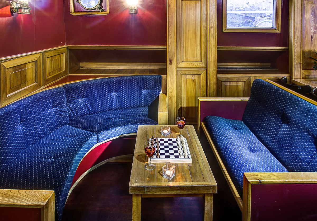Salotto interno con tavolo da scacchi, divani blu e decorazioni in legno lucido.