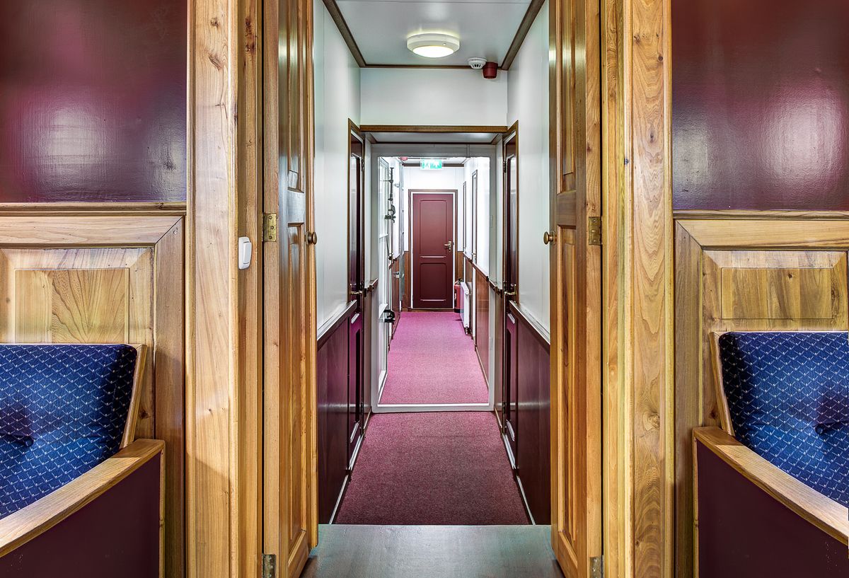 Corridoio interno stretto della nave con pannelli in legno e moquette rossa.