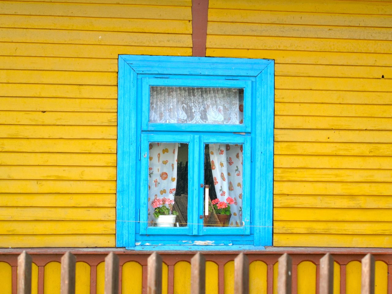Finestra decorata in azzurro su casa in legno gialla a Zalipie, villaggio artistico della Polonia.