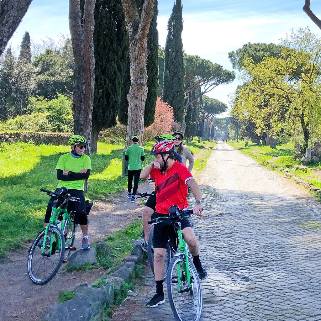 Radfahrer auf Reisen mit Girolibero auf der Via Appia Antica in Rom, Italien – Radfahrer genießen eine Tour entlang der historischen Via Appia Antica, umgeben von Zypressen und römischen Ruinen.