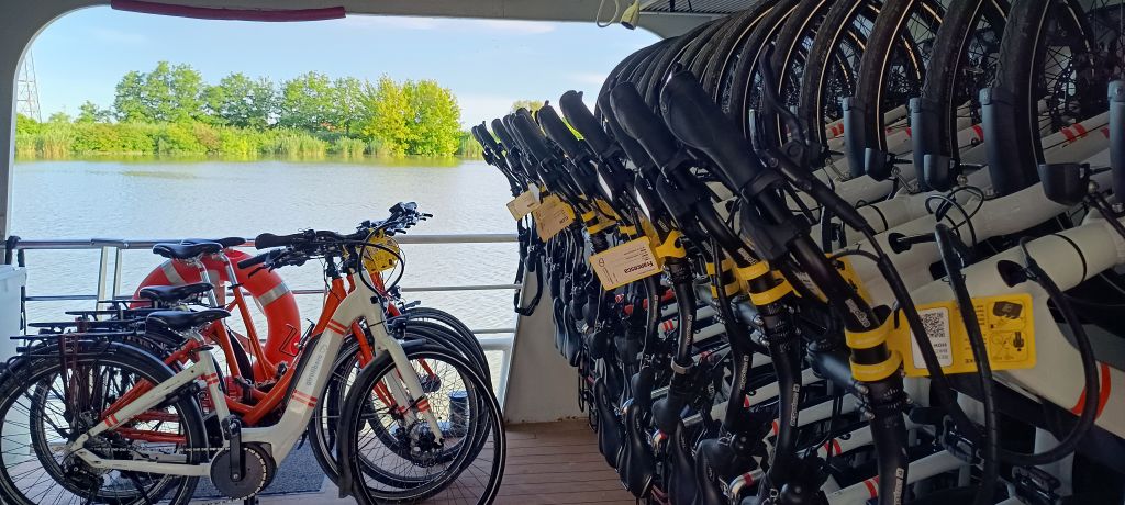 Bicycles resting on the outside deck of a barge, in a rural landscape with green meadows and trees