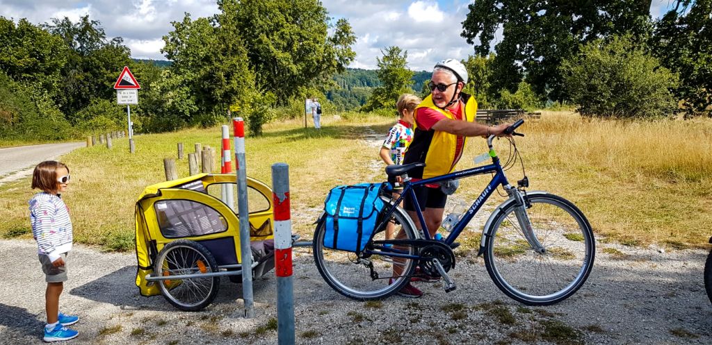 Papà in bici con carrello per bambini attraversa una passaggio tra due pali sulla ciclabile, Germania.