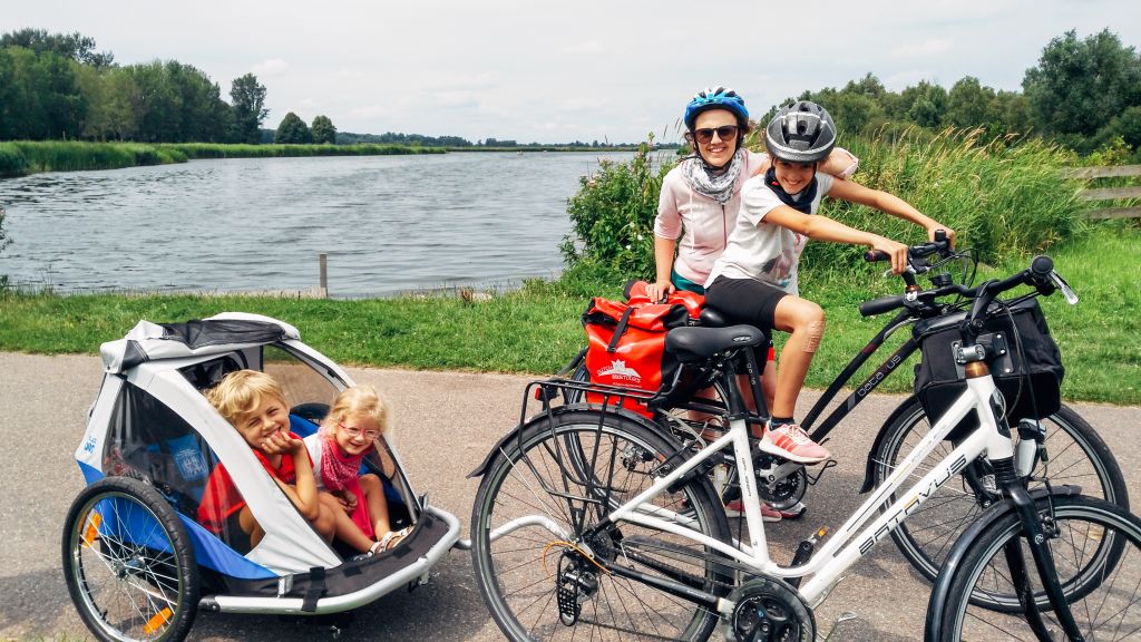 Ciclista su un sentiero vicino a un fiume con vegetazione in Olanda, bici con carretto, vacanze in famiglia all'aria aperta