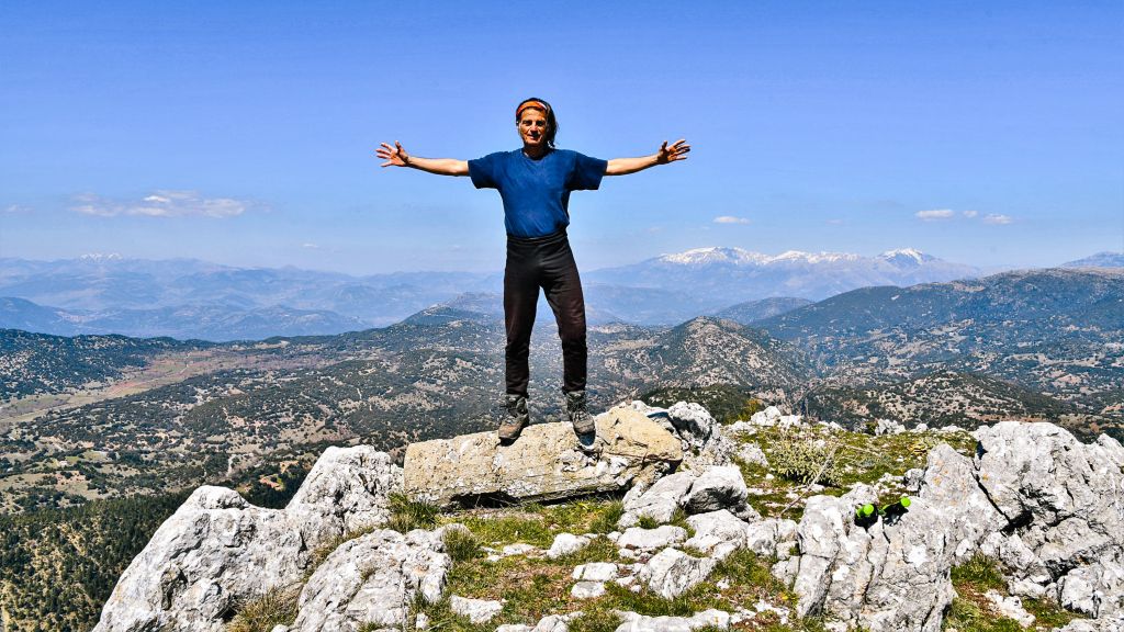 Persona su una cima rocciosa che ammira il paesaggio montuoso del Peloponneso.