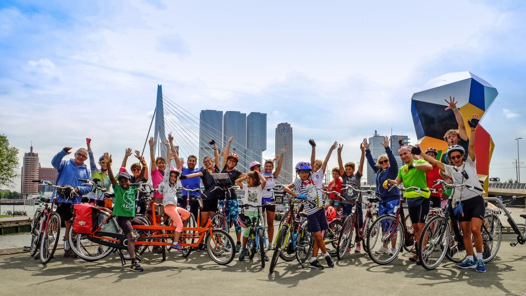 Gruppo numeroso di ciclisti con bici Girolibero fa una foto ricordo con lo skyline di una moderna città olandese sullo sfondo