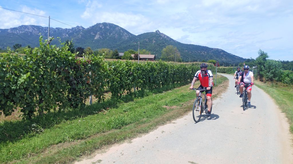 Ciclisti su pista ciclabile tra meleti e vigneti ai piedi delle Alpi Marittime.