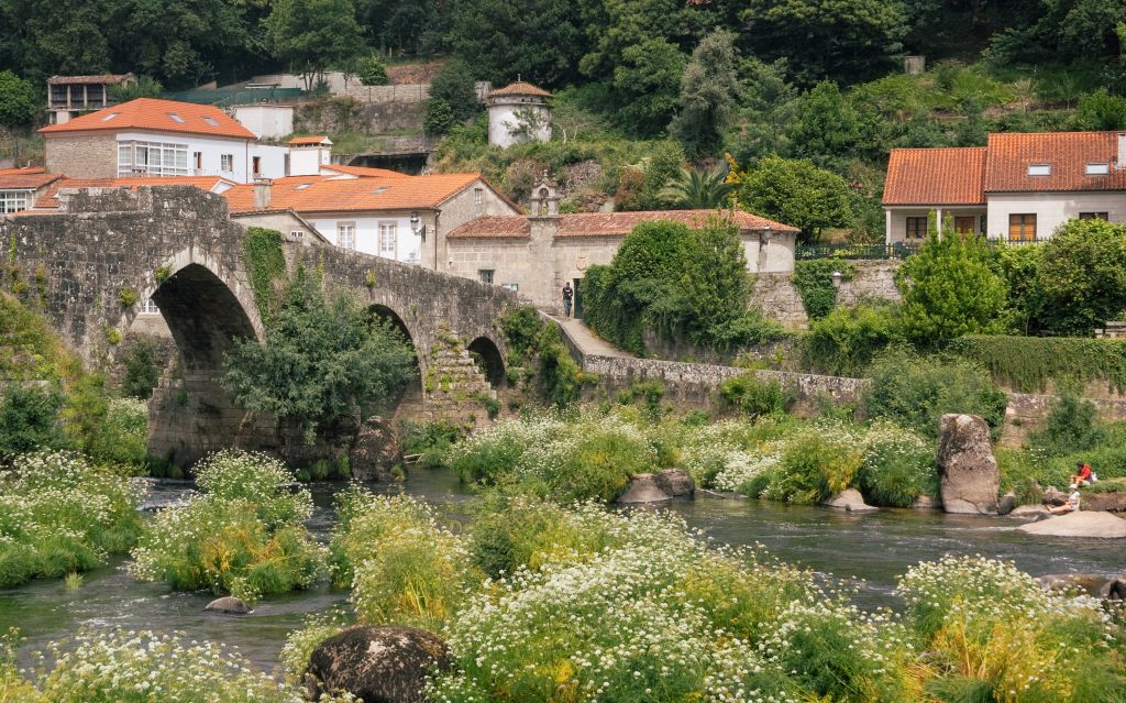 Veduta di un villaggio rurale circondato da verde con ponte antico in pietra lungo il Cammino di Santiago.