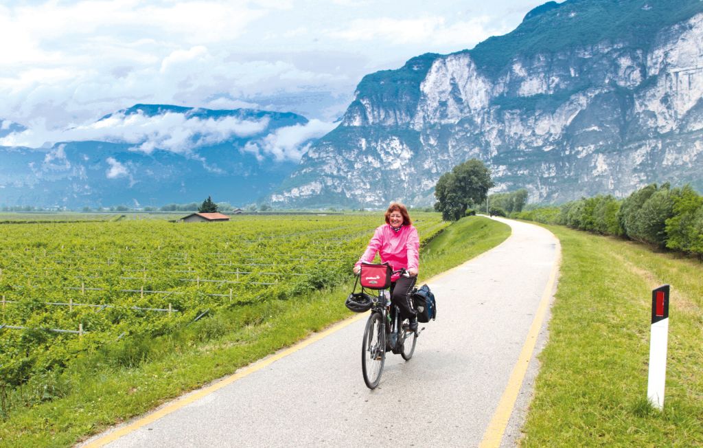 Woman cycling on the Adige Cycle Path with the Dolomites in the background.
