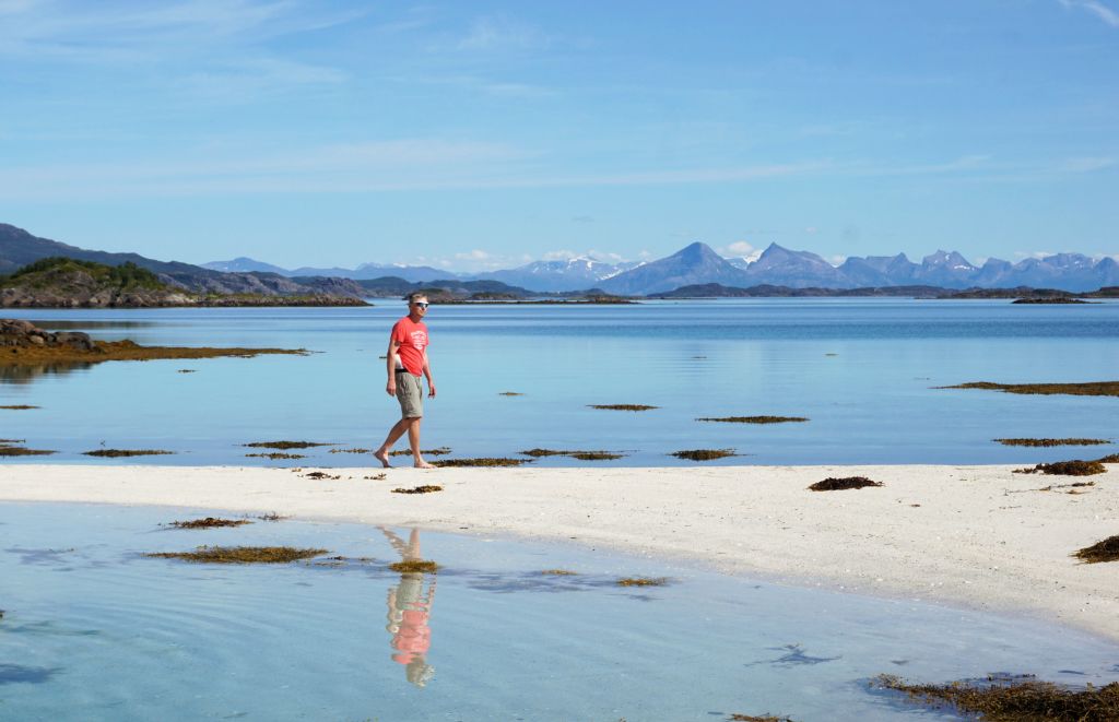 Persona che cammina su una spiaggia sabbiosa con basse maree e montagne in lontananza.