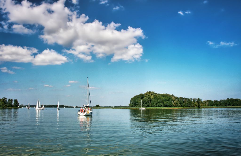 Barca a vela su un lago limpido nei Laghi Masuri, Polonia, con cielo azzurro e nuvole bianche.
