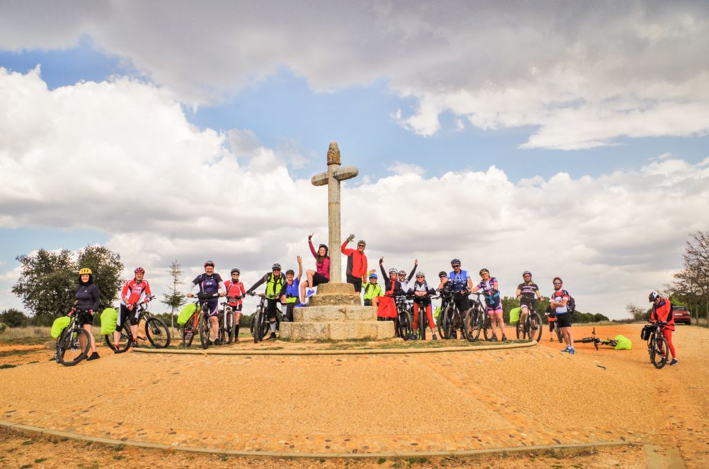 Gruppo di ciclisti in viaggio con Girolibero sul Cammino di Santiago, fermi per una foto di gruppo vicino a una grande croce