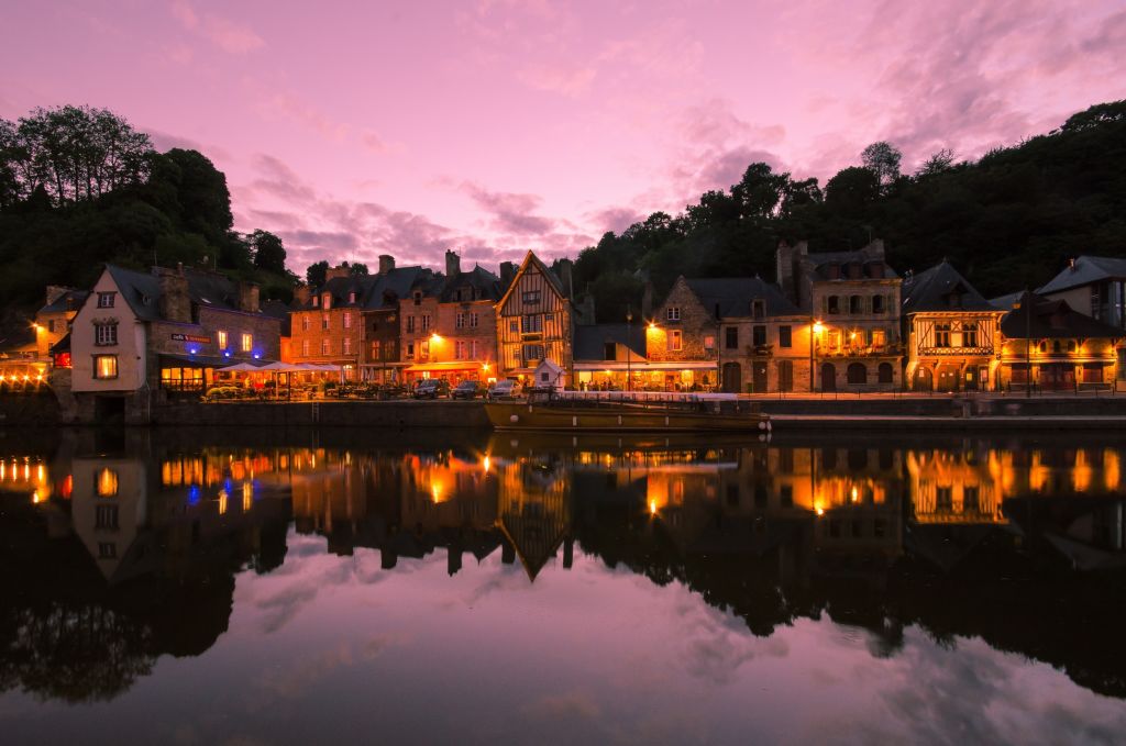 Tramonto riflesso su un fiume nella città di Dinan, Bretagna, Francia, con antiche case lungo la riva.