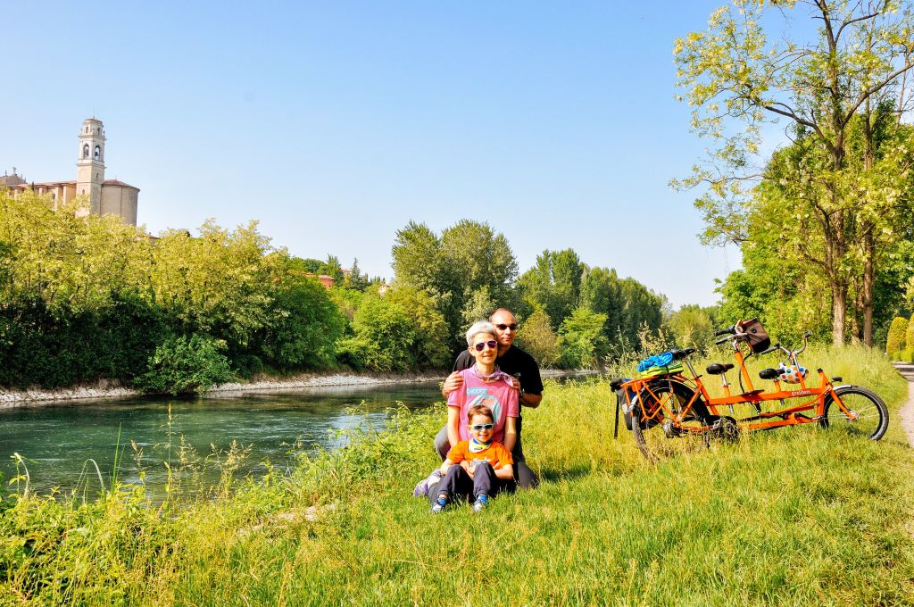 Famiglia di cicloturisti seduta su un prato lungo il fiume, occhiali da sole, family tandem, zona termale di Padova