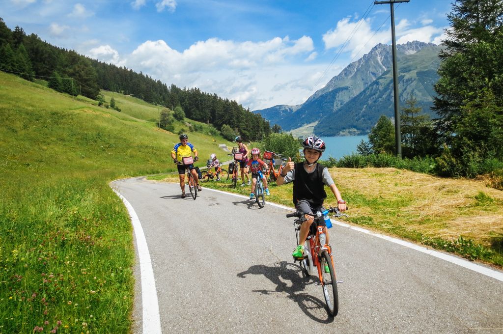 Family riding along the Venosta Valley cycle path with view of the South Tyrolean mountains.