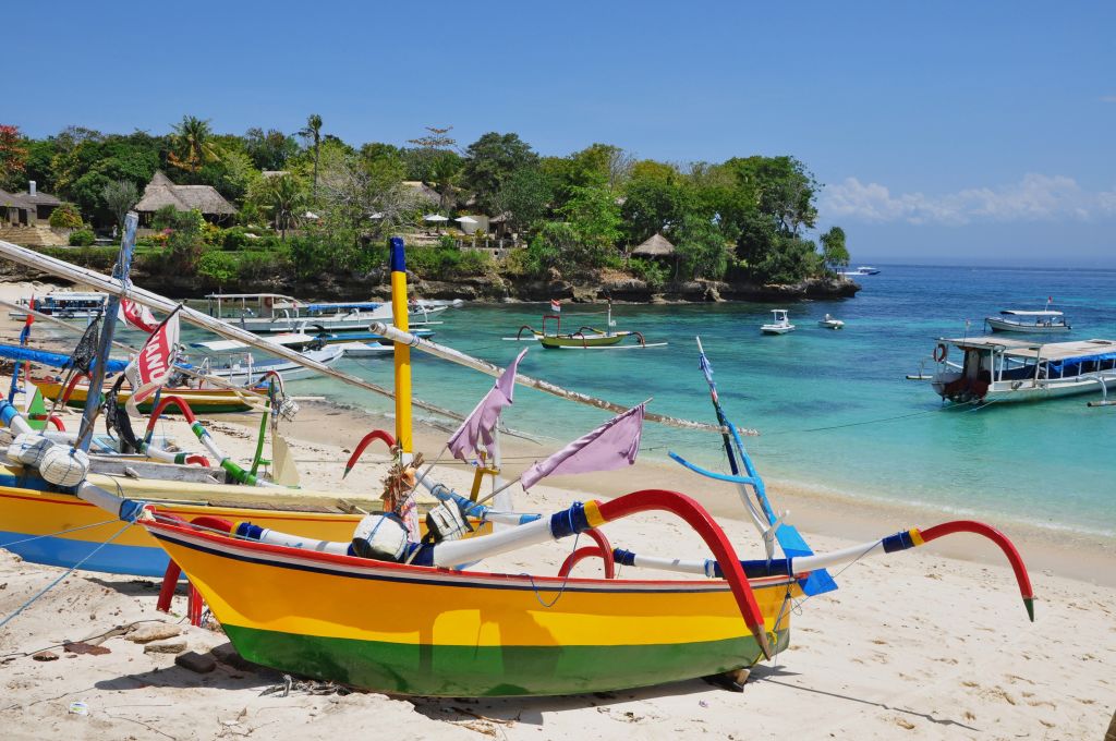 Spiaggia e barche a Bali – Barca colorata tipica balinese ormeggiata su una spiaggia con palme e acque cristalline.