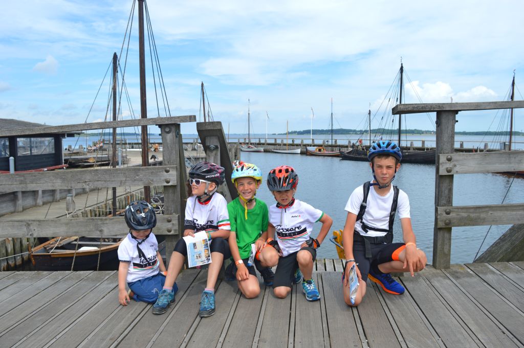 Gruppo di bambini in posa su un pontile in legno con barche a vela ormeggiate a Helsingør, Danimarca, viaggi in bici per famiglie "Girolibero"