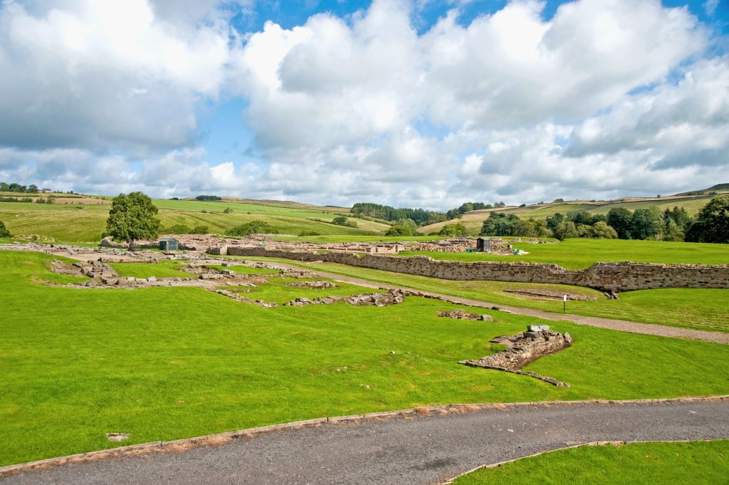 Distese verdi con resti del Vallo di Adriano sotto un cielo nuvoloso.