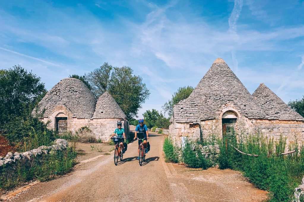 Cyclist crossing a rural village, traditional trulli surrounded by countryside and blue skies, Alberobello, Apulia