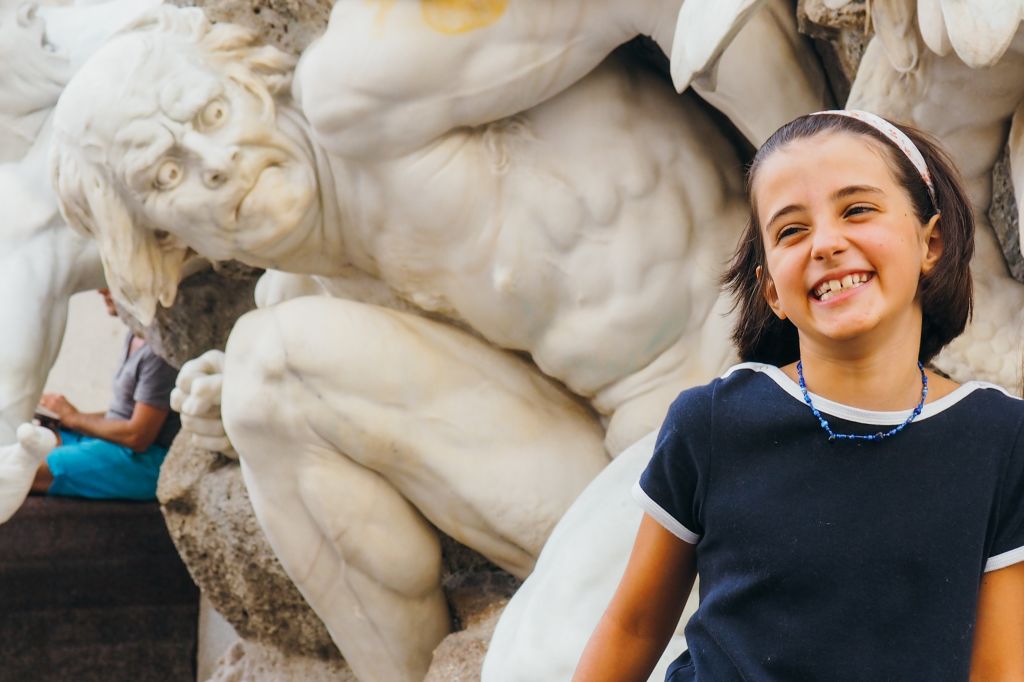 Bambina sorridente davanti alla statua di una creatura mitologica, ciclabile del Danubio da Linz a Vienna, Austria