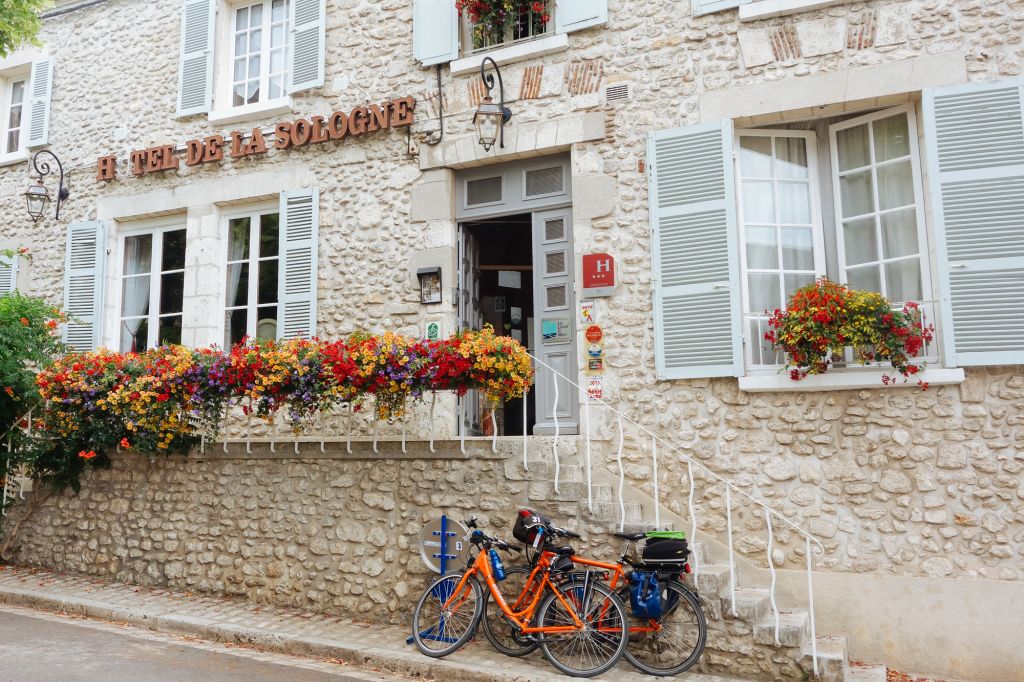 Edificio tipico in pietra con fiori e biciclette "Girolibero" parcheggiate, Francia.