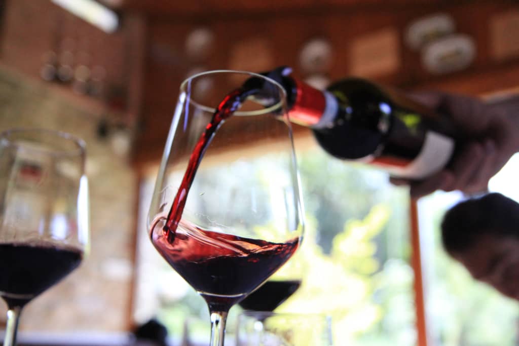 Primo piano di un bicchiere di vetro in cui viene versato da parte di un sommelier il Barolo, vacanza in bici, Piemonte