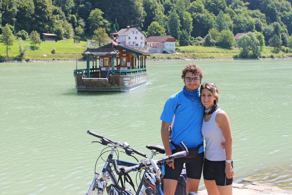 Coppia con biciclette sulla riva del fiume Inn a Passau, davanti alla famosa locanda sull’acqua.