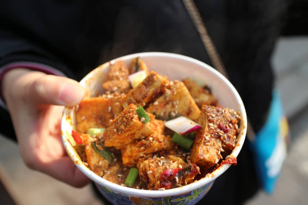 Ciotola di street food cinese con tofu speziato e verdure, servita calda per strada.