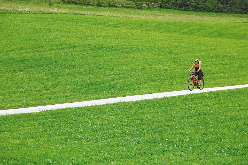 Ciclista che pedala su un sentiero ciclabile tra i prati verdi nella regione di Salisburgo.