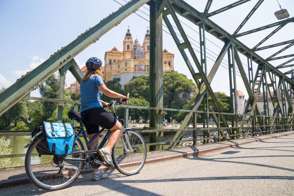 Cicloturista con caschetto mentre osserva l'abbazia di Melk, borse da bici, fiume Danubio, vacanza in bici, Austria