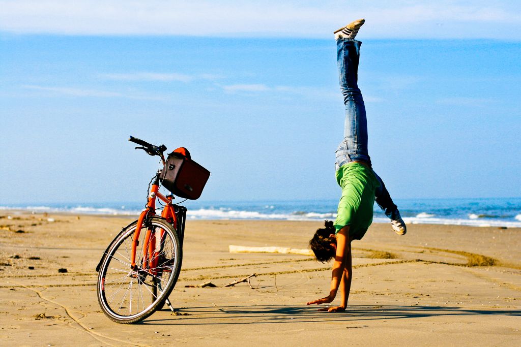 Ciclista in spiaggia intenta a fare una verticale accanto alla bici muscolare Girolibero, vacanza tra Venezia e Parenzo