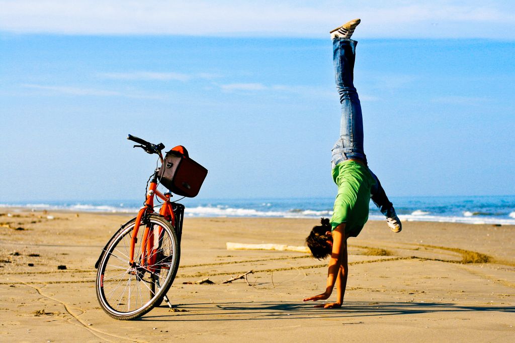 Ciclista in spiaggia intenta a fare una verticale accanto alla sua bici "Girolibero", vacanza in bicicletta tra Venezia e Parenzo