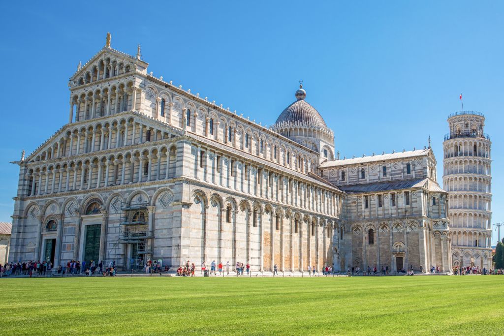Piazza del Duomo, cattedrale e torre pendente di Pisa, cupola, prato verde, fila di turisti, visitare la Toscana in bici