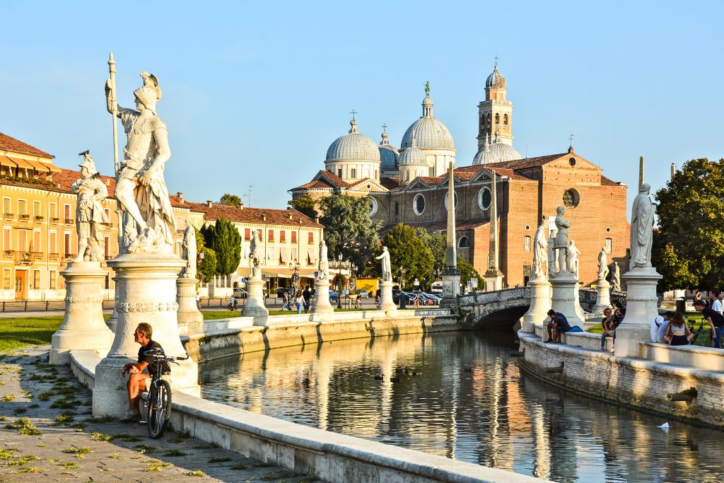 Ciclista in sosta tra le statue di Prato della Valle con vista sulla Basilica di Santa Giustina a Padova