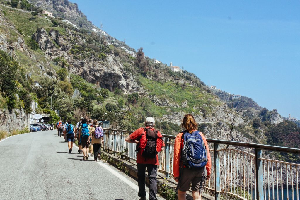 Gruppo di viaggiatori a piedi, paesaggio roccioso e verde, trekking nella Costiera Amalfitana, slow tourism, Campania