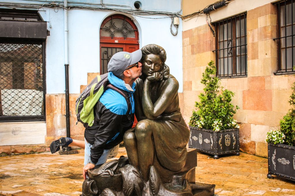 Camminatore che abbraccia una statua in bronzo di un pellegrino con bastone, simbolo dell’esperienza del cammino.